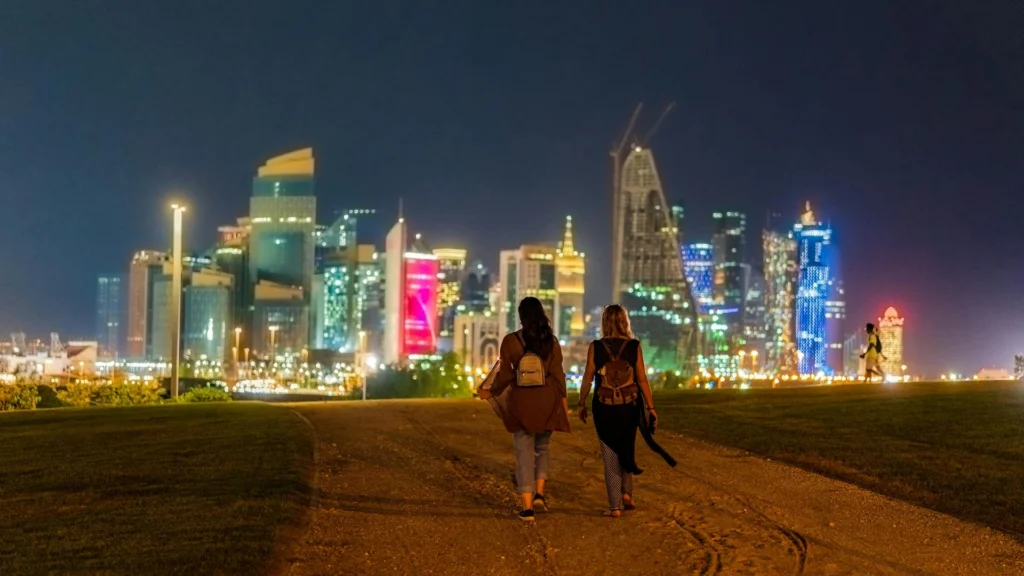 Anonymous women walking in city near illuminated skyscrapers at night